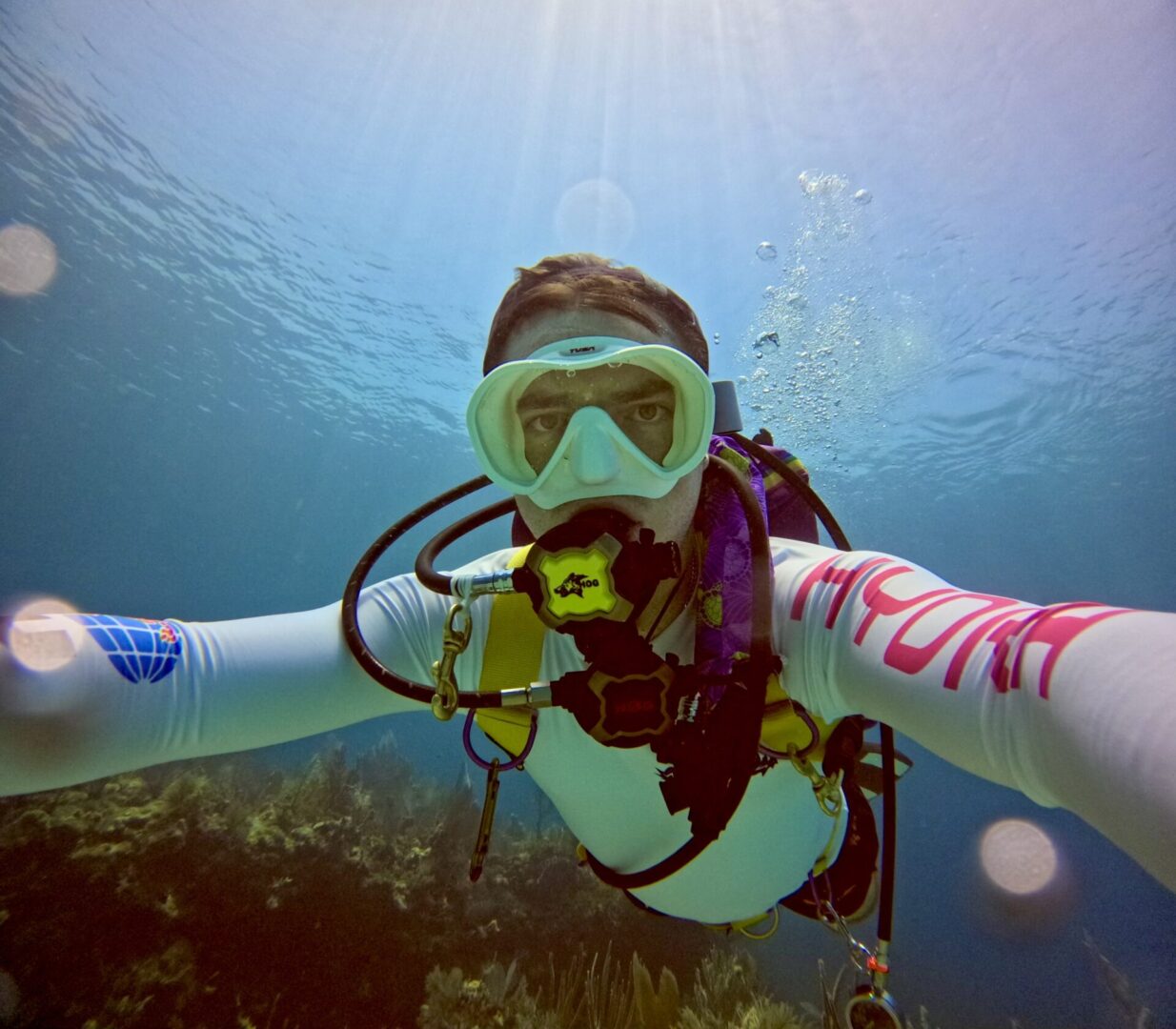 A person in scuba gear is underwater with the sun shining.